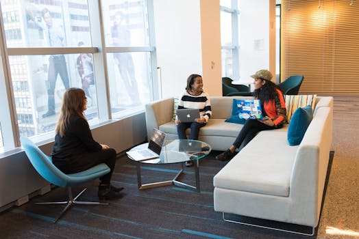 Three women engaged in a meeting with laptops in a bright, modern office setting.